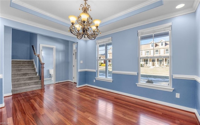 empty room with a tray ceiling, wood-type flooring, stairway, an inviting chandelier, and ornamental molding