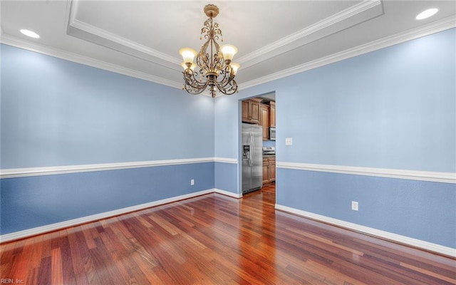 spare room featuring a notable chandelier, wood finished floors, baseboards, a raised ceiling, and crown molding