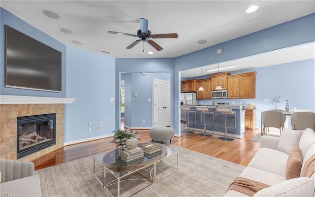 living room with recessed lighting, light wood-type flooring, a tile fireplace, and baseboards