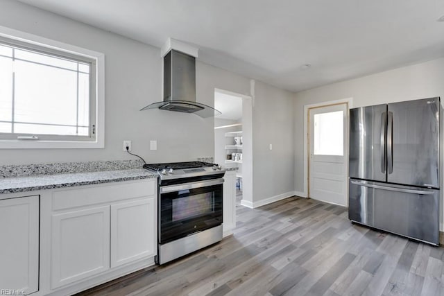 kitchen with appliances with stainless steel finishes, white cabinetry, light stone countertops, light wood-type flooring, and wall chimney exhaust hood