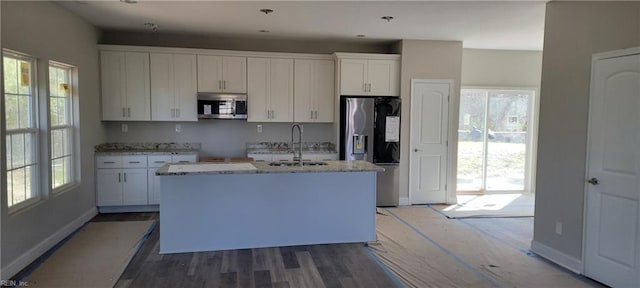 kitchen with a kitchen island with sink, stainless steel appliances, wood finished floors, a sink, and white cabinets