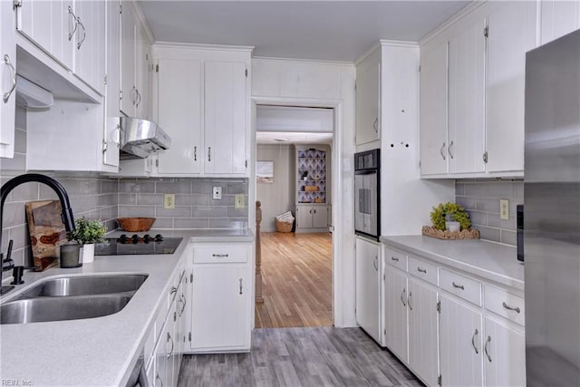 kitchen featuring light countertops, a sink, freestanding refrigerator, and under cabinet range hood