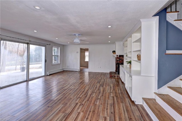 unfurnished living room with stairs, baseboard heating, a fireplace, and wood finished floors