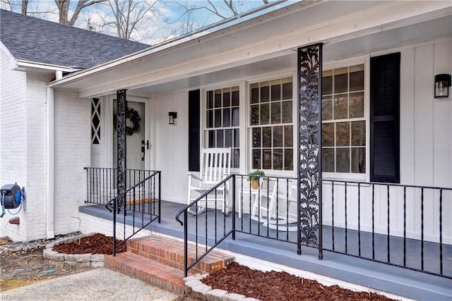 entrance to property featuring covered porch, brick siding, and a shingled roof