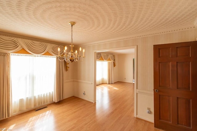 empty room with light wood-style floors, visible vents, and an inviting chandelier