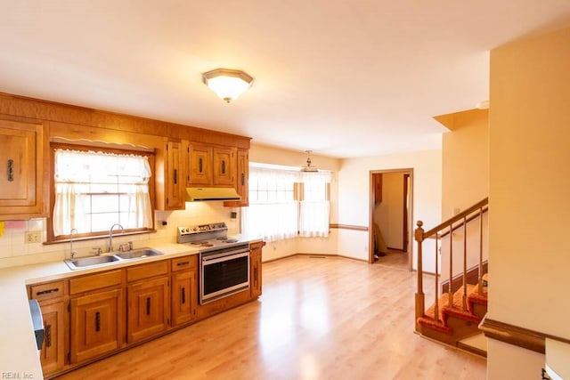 kitchen with under cabinet range hood, a sink, light wood-type flooring, brown cabinets, and stainless steel electric range oven