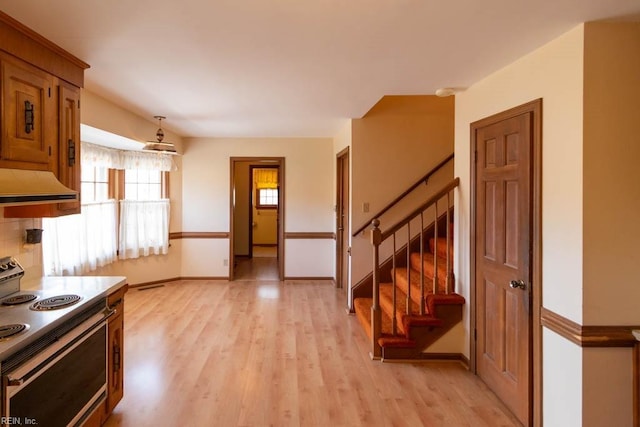 kitchen featuring electric range, baseboards, light wood-style flooring, brown cabinets, and exhaust hood