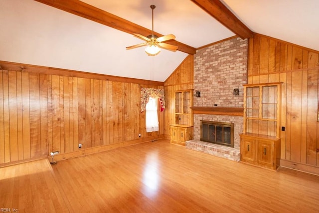 unfurnished living room with vaulted ceiling with beams, wood walls, a brick fireplace, and wood finished floors