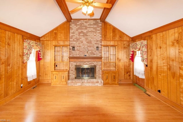 unfurnished living room with plenty of natural light, a brick fireplace, vaulted ceiling with beams, and wood finished floors