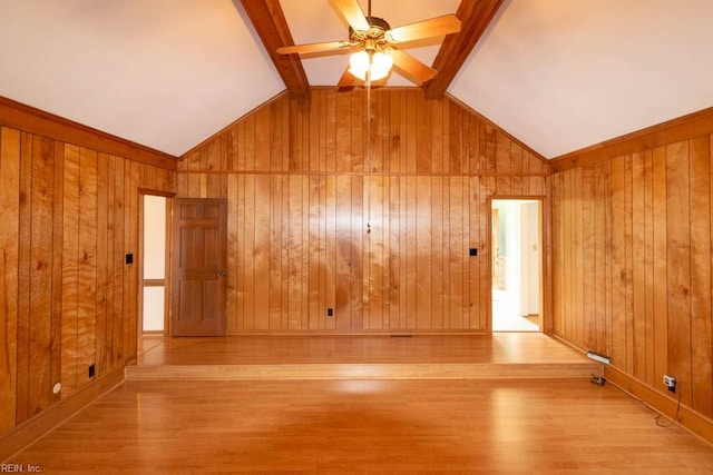 empty room with a ceiling fan, vaulted ceiling with beams, wooden walls, and wood finished floors