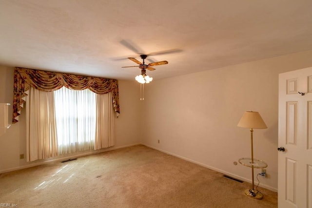 empty room featuring a ceiling fan, visible vents, light carpet, and baseboards