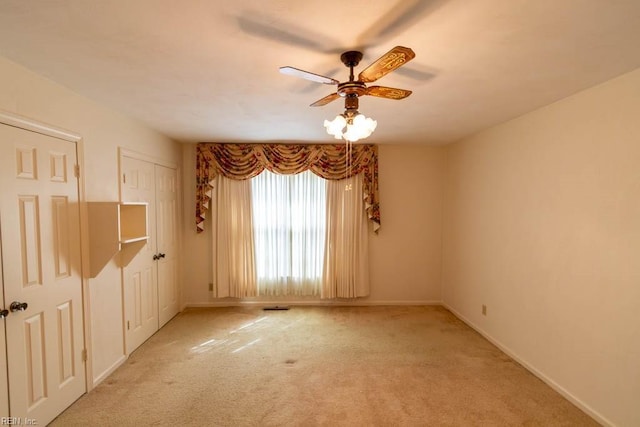 empty room with visible vents, baseboards, a ceiling fan, and light colored carpet