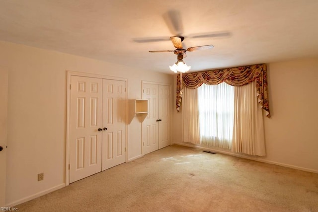 unfurnished bedroom featuring ceiling fan, carpet flooring, two closets, and baseboards