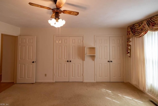 unfurnished bedroom featuring multiple closets, visible vents, a ceiling fan, light carpet, and baseboards