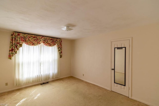 empty room featuring baseboards, visible vents, and light colored carpet