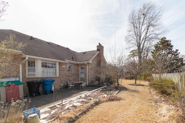 rear view of house featuring a shingled roof, a chimney, a patio, and brick siding