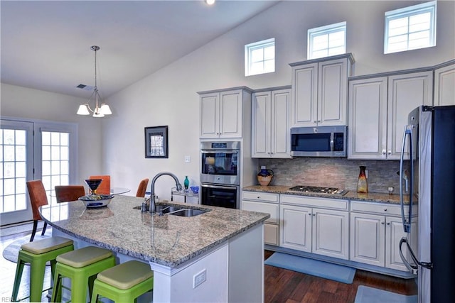 kitchen with light stone counters, a breakfast bar, dark wood-style flooring, stainless steel appliances, and a sink