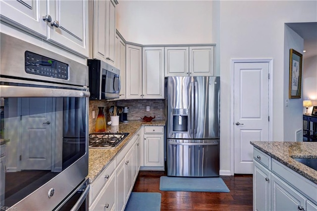 kitchen with appliances with stainless steel finishes, dark wood-type flooring, decorative backsplash, and light stone countertops