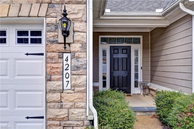 doorway to property featuring stone siding and roof with shingles