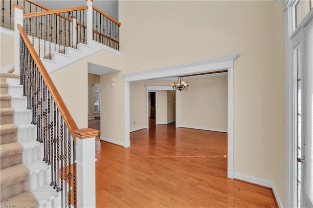 foyer with light wood-type flooring, an inviting chandelier, a high ceiling, and baseboards