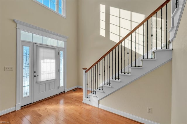 foyer entrance featuring wood-type flooring, a towering ceiling, baseboards, and stairs