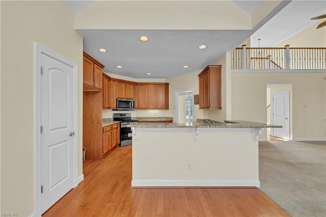 kitchen featuring a peninsula, appliances with stainless steel finishes, brown cabinetry, and light stone counters