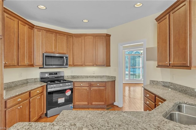 kitchen featuring light stone countertops, appliances with stainless steel finishes, a sink, and recessed lighting