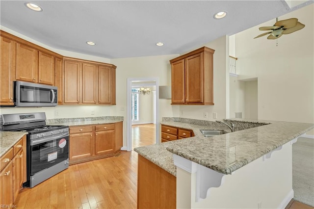 kitchen featuring light wood finished floors, appliances with stainless steel finishes, a peninsula, light stone countertops, and a sink