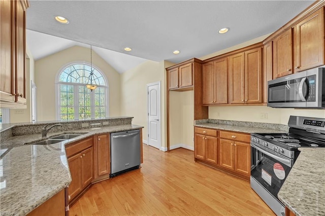 kitchen with stainless steel appliances, a sink, brown cabinets, light stone countertops, and light wood finished floors