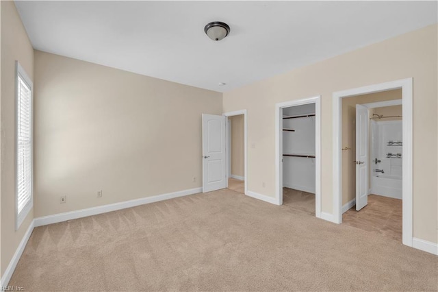 unfurnished bedroom with light carpet, a closet, a walk in closet, and baseboards