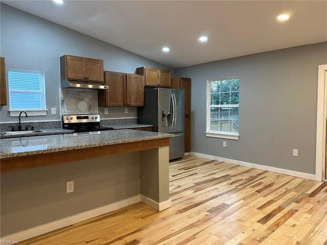 kitchen with under cabinet range hood, a sink, vaulted ceiling, appliances with stainless steel finishes, and dark stone countertops