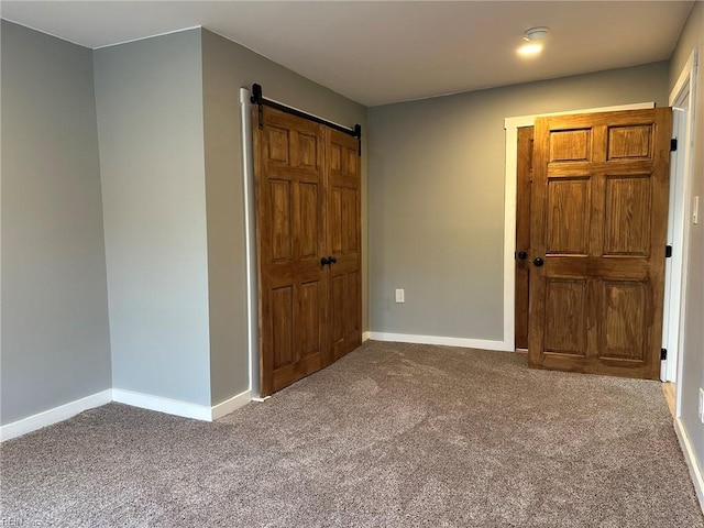 unfurnished bedroom featuring carpet flooring, baseboards, and a barn door