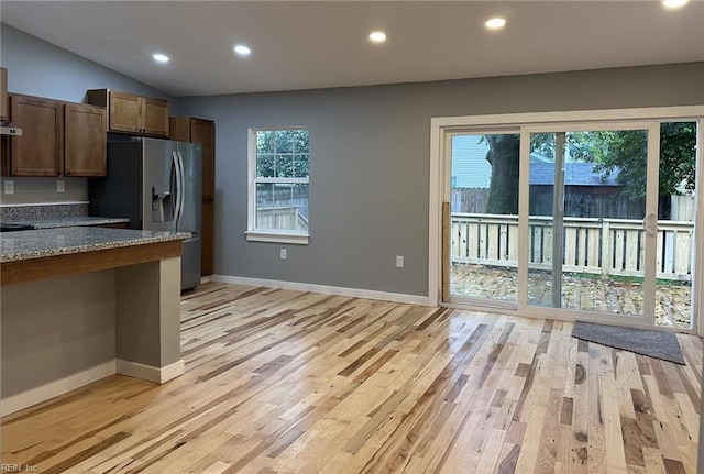 kitchen with stainless steel refrigerator with ice dispenser, recessed lighting, lofted ceiling, light wood-style flooring, and baseboards