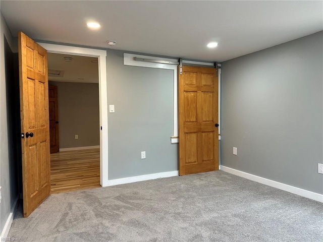 empty room featuring light carpet, a barn door, baseboards, and recessed lighting