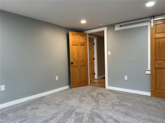 spare room featuring carpet floors, a barn door, baseboards, and recessed lighting