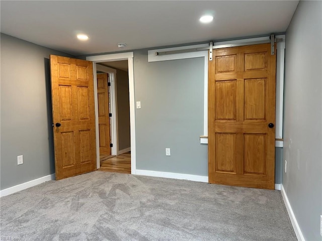 unfurnished bedroom with carpet floors, a barn door, and baseboards