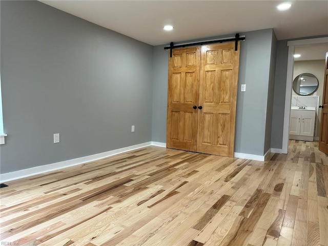 unfurnished bedroom featuring light wood finished floors, a barn door, visible vents, and baseboards