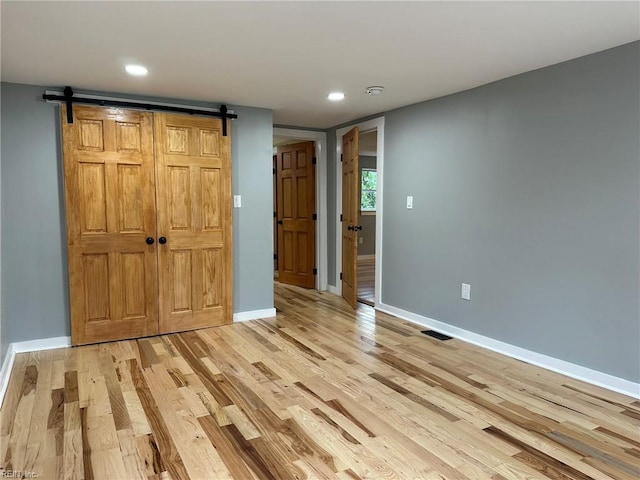 unfurnished bedroom featuring a barn door, visible vents, baseboards, light wood-style flooring, and recessed lighting