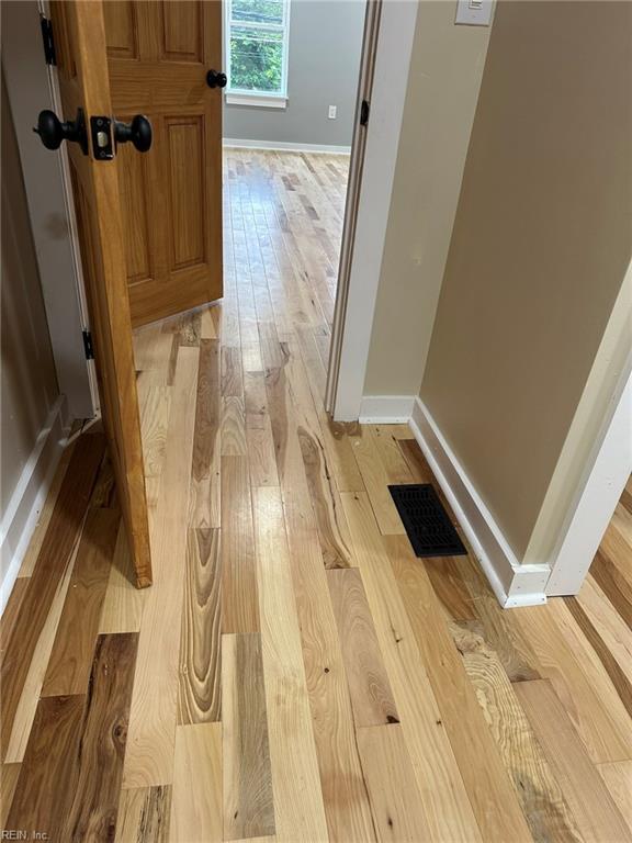 hallway with light wood-style floors, baseboards, and visible vents