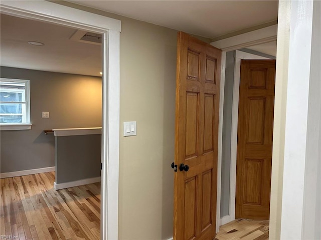 hallway featuring light wood-style floors, baseboards, and an upstairs landing