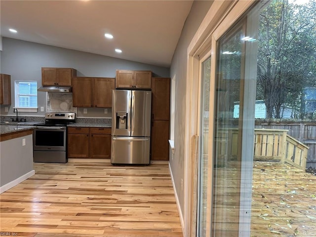 kitchen featuring brown cabinets, light wood finished floors, lofted ceiling, appliances with stainless steel finishes, and under cabinet range hood