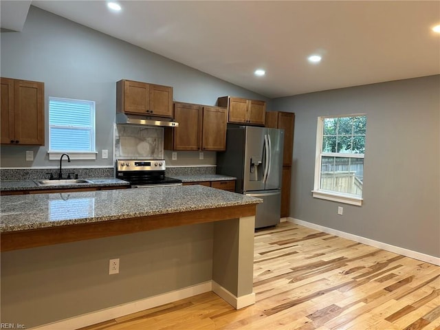 kitchen with stainless steel appliances, lofted ceiling, a sink, dark stone countertops, and under cabinet range hood