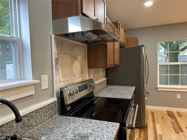 kitchen with under cabinet range hood, baseboards, brown cabinets, light wood finished floors, and stainless steel range with electric stovetop