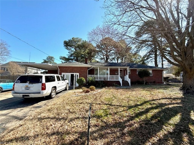 ranch-style house featuring brick siding, covered porch, concrete driveway, a front yard, and a carport