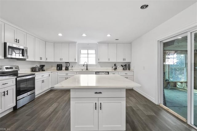 kitchen featuring dark wood-type flooring, a sink, light countertops, appliances with stainless steel finishes, and a center island