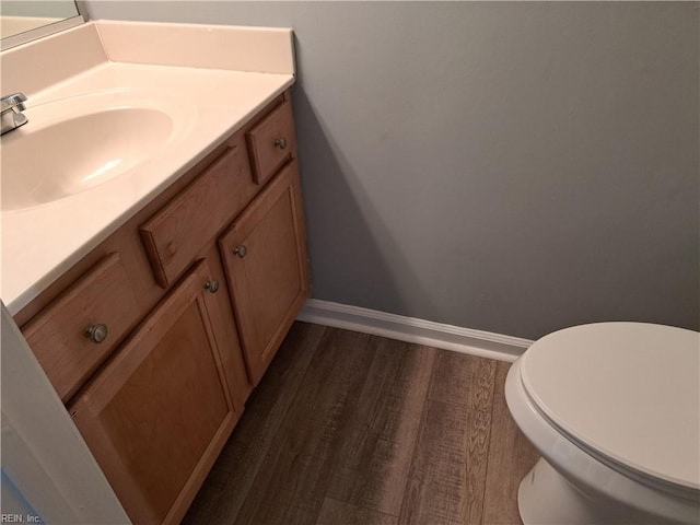 bathroom featuring toilet, baseboards, wood finished floors, and vanity