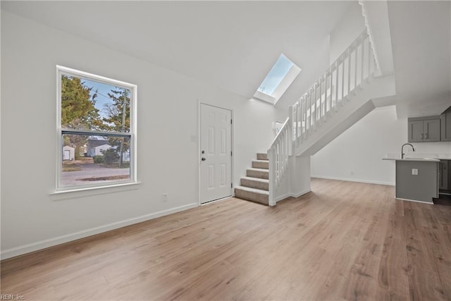 unfurnished living room featuring stairway, a skylight, light wood-style flooring, and baseboards