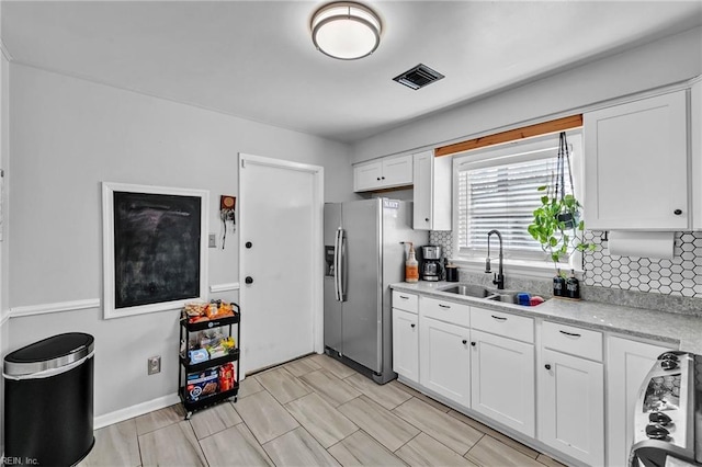 kitchen with a sink, visible vents, white cabinetry, light countertops, and stainless steel fridge