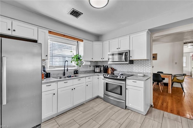 kitchen featuring visible vents, backsplash, appliances with stainless steel finishes, white cabinets, and a sink