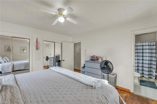 bedroom featuring connected bathroom, wood finished floors, a ceiling fan, baseboards, and multiple closets